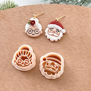 May include: A set of four Christmas-themed earrings and cookie cutters. The earrings feature Santa Claus and a woman with a red flower in her hair. The cookie cutters are also of Santa Claus and the woman.