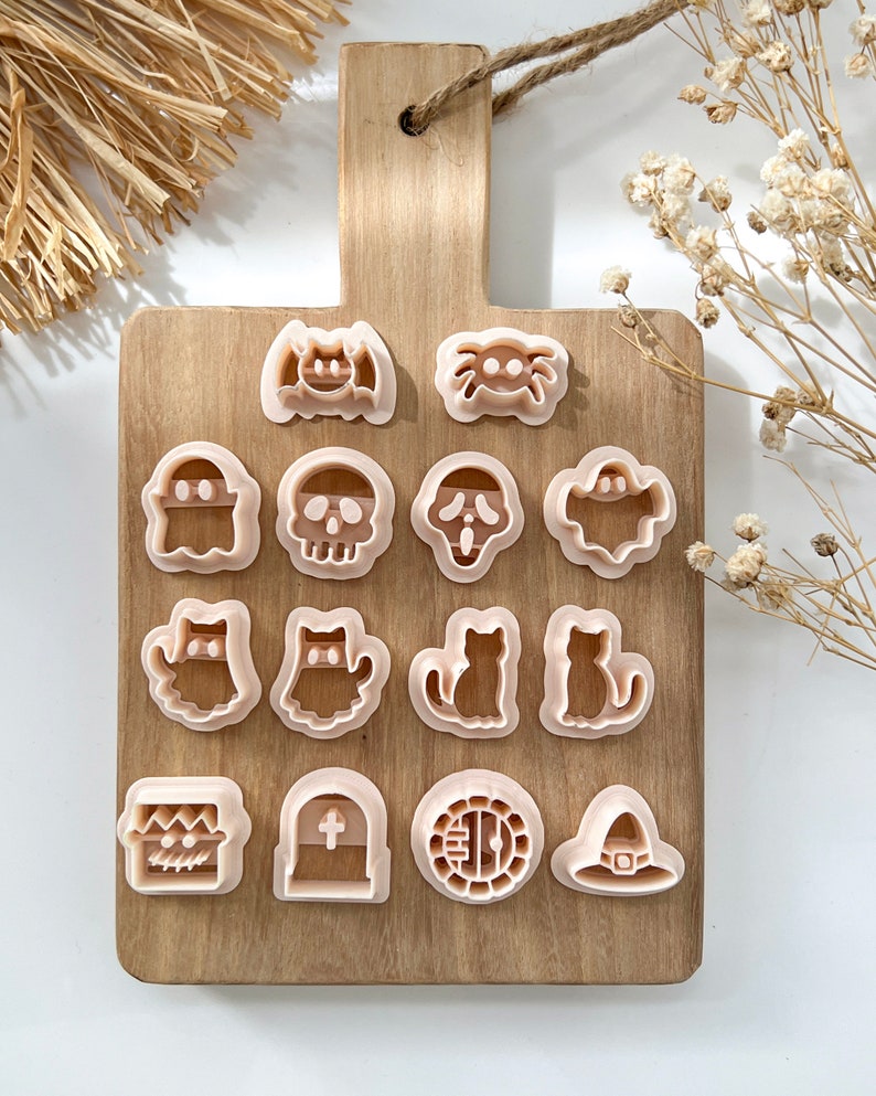 Pu&ograve; includere: Un set di 16 stampini per biscotti a tema Halloween su un tagliere di legno. Gli stampini hanno la forma di un fantasma, un teschio, un pipistrello, un ragno, un gatto, un cappello da strega, una lapide e altro ancora.
