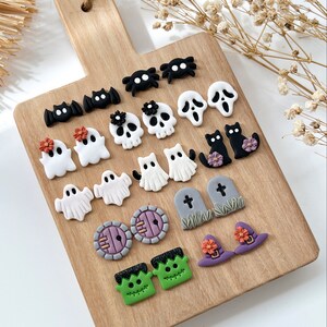 Pu&ograve; includere: Un tagliere di legno con una variet&agrave; di orecchini in pasta polimerica a tema Halloween. Gli orecchini includono fantasmi, pipistrelli, ragni, teschi, gatti, cappelli da strega, lapidi e Frankenstein.
