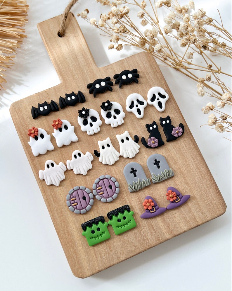 Pu&ograve; includere: Un tagliere di legno con una variet&agrave; di orecchini in pasta polimerica a tema Halloween. Gli orecchini includono fantasmi, pipistrelli, ragni, teschi, gatti, cappelli da strega, lapidi e Frankenstein.
