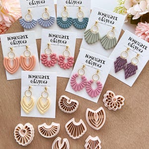 May include: A collection of polymer clay earrings in various colors, including blue, pink, and green, displayed on white cards. The earrings feature gold-colored hoops and decorative designs. The image also shows several clay cutters in matching shapes. The text "loseaux clayco" is printed on the cards.