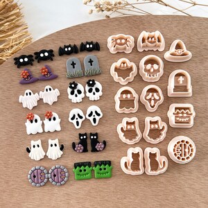 Pu&ograve; includere: Un set di 20 tagliabiscotti a tema Halloween, tra cui fantasmi, pipistrelli, ragni, gatti, zucche e altro ancora. I tagliabiscotti sono in plastica beige chiaro e sono disposti su una superficie di legno.