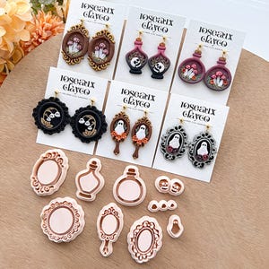 Puede incluir: Una colección de pendientes de arcilla polimérica hechos a mano con varios diseños, incluyendo setas, calaveras y fantasmas. Los pendientes se muestran en tarjetas blancas con la marca "Roseaux Clayco".