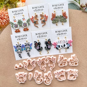 May include: Polymer clay earrings in various animal designs, such as raccoons, butterflies, and cows, displayed on white cards. The earrings feature vibrant colours and intricate details, with matching clay cutters also visible.