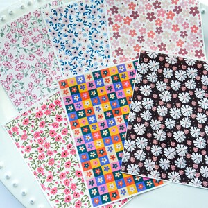 May include: Six sheets of patterned paper with floral designs. The patterns include pink and white flowers, blue and white flowers, red, yellow, blue, and green flowers in a chequered pattern, pink and white flowers on a brown background, and pink and white flowers on a green background.