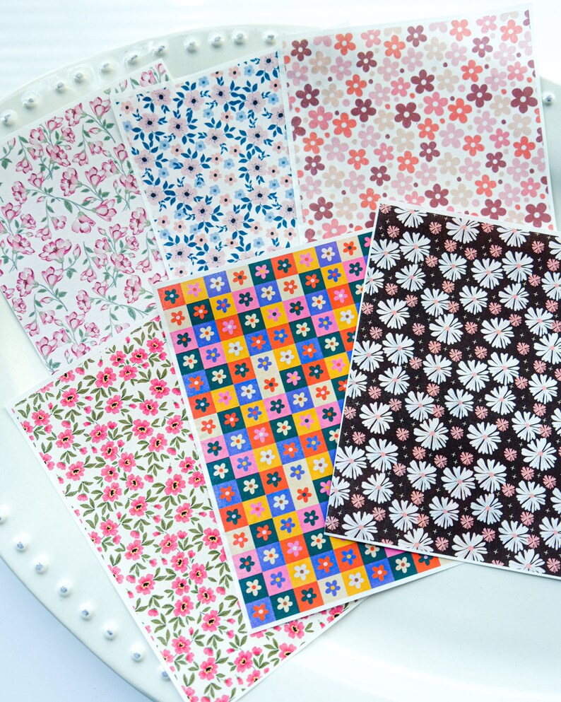 May include: Six sheets of patterned paper with floral designs. The patterns include pink and white flowers, blue and white flowers, red, yellow, blue, and green flowers in a chequered pattern, pink and white flowers on a brown background, and pink and white flowers on a green background.
