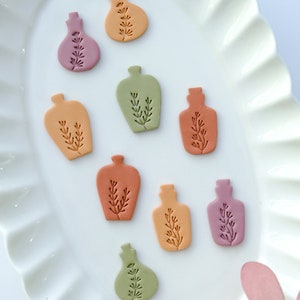 May include: Nine small ceramic bottles in various shades of orange, pink, and green. Each bottle has a simple floral design.