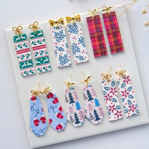 May include: A selection of Christmas-themed earrings featuring various patterns, including plaid, snowflakes, holly, and trees. The earrings are made with gold-coloured metal and have a bow detail.
