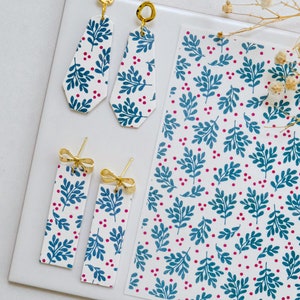 May include: A pair of dangle earrings and a pair of stud earrings with a white background and a blue and pink floral pattern. The earrings are made of polymer clay and have gold accents.