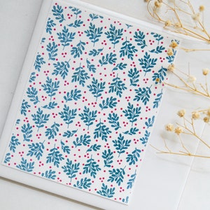 May include: A white card with a repeating pattern of teal blue leaves and small pink dots. The card is on a white surface.
