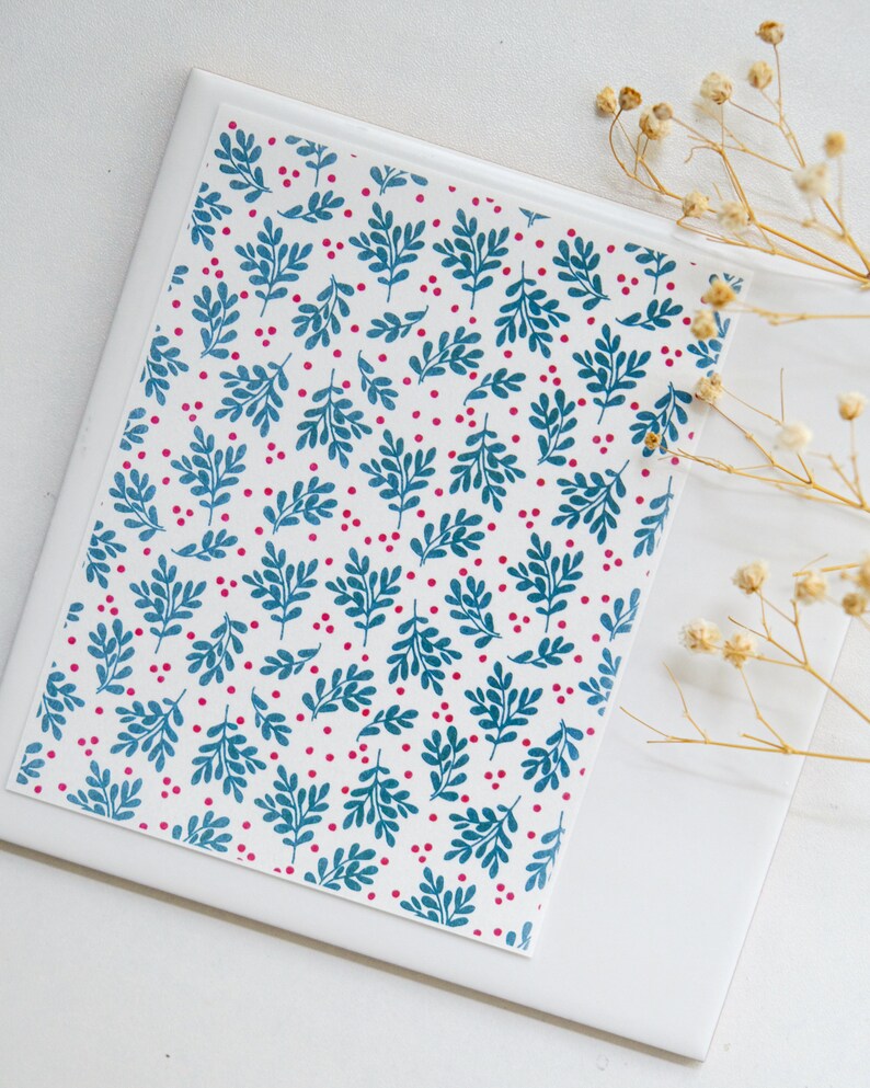 May include: A white card with a repeating pattern of teal blue leaves and small pink dots. The card is on a white surface.