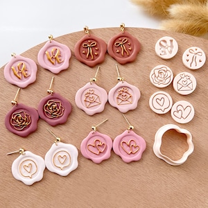 May include: Assortment of pink and white polymer clay earrings with gold accents. The earrings feature various designs including hearts, roses, letters, and envelopes. There are also several polymer clay cutters in the image, including a heart, a rose, and a circle.