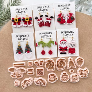 May include: A selection of Christmas-themed polymer clay earrings featuring Santa, Mrs. Claus, Christmas trees, and bow designs. The earrings are presented on white cards with the brand name "10seaux clayco". Cookie cutters in festive shapes are also visible.