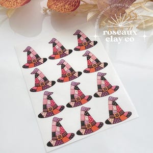 May include: A white sheet featuring eleven printed witch hat designs in a patchwork style. Each hat displays a variety of patterns including polka dots, gingham, and solid colors in shades of purple, pink, and orange, with a brown buckle detail.