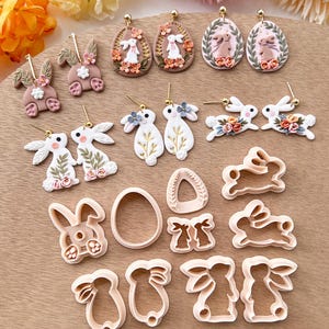 May include: A set of 12 polymer clay bunny and egg earrings and cookie cutters. The earrings feature bunnies with floral accents and eggs with floral wreaths. The cookie cutters are in the shapes of bunnies and eggs.