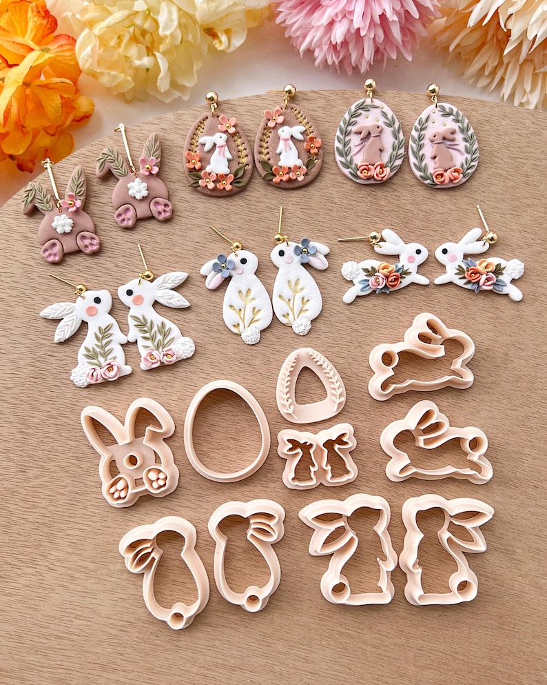 May include: A set of 12 polymer clay bunny and egg earrings and cookie cutters. The earrings feature bunnies with floral accents and eggs with floral wreaths. The cookie cutters are in the shapes of bunnies and eggs.
