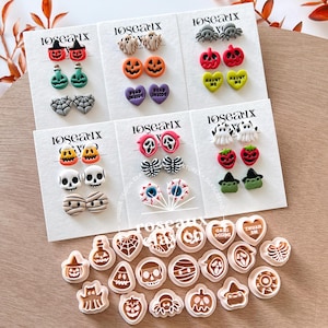 May include: A collection of Halloween-themed polymer clay stud earrings displayed on six white cards branded with the text Roseaux. The set includes shapes like pumpkins, ghosts, skulls, spiders, hearts with text, and eyeballs, alongside matching plastic cutters.