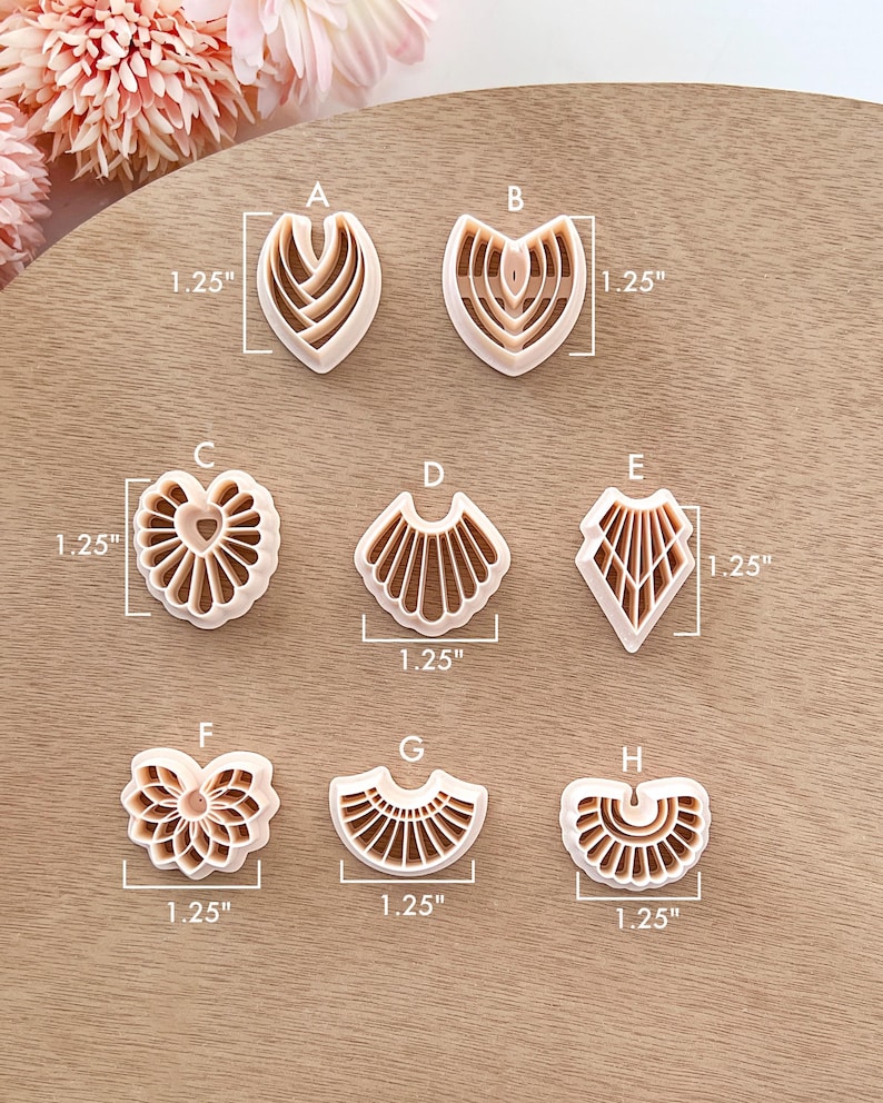May include: A collection of eight beige polymer clay cutters in various shapes, each measuring 1.25 inches. Designs include heart, fan, and geometric patterns, ideal for crafting. The cutters are arranged on a light brown wooden surface.