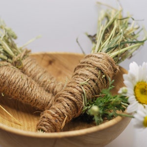May include: Two bundles of dried grass wrapped in twine, sitting in a wooden bowl with a white daisy flower.