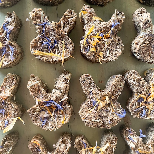 Könnte beinhalten: Eine Sammlung handgemachter Hasen-Leckerlis aus getrockneten Kräutern und Blumen. Die Leckerlis sind hellbraun und haben verschiedene violette und gelbe Blüten eingebettet.