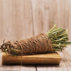 May include: A bunch of dried grass tied together with twine and placed on a wooden surface.