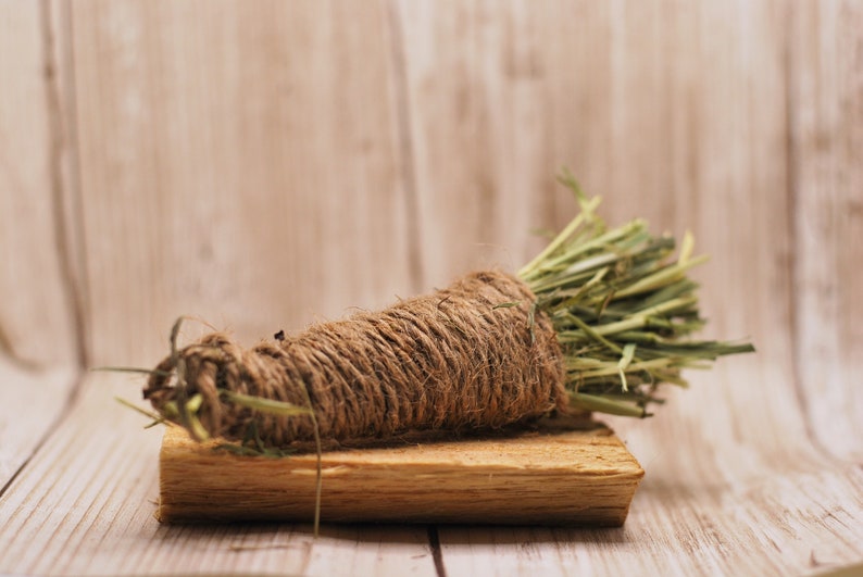 May include: A bunch of dried grass tied together with twine and placed on a wooden surface.