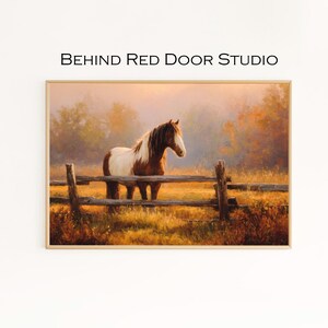 May include: A framed painting depicting a horse in a field, with a wooden fence in the foreground. The horse is brown and white, and the painting has a warm, golden colour palette. The text "BEHIND RED DOOR STUDIO" is at the top.