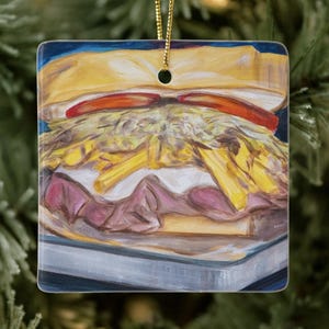 May include: Square ceramic Christmas ornament featuring a colorful painting of a sandwich. The sandwich has layers of meat, cheese, and french fries, with two red tomato slices on top. A gold string is attached for hanging.