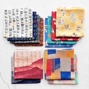 May include: A collection of square fabric cloths featuring diverse patterns including Korean Hangul script, traditional floral motifs, geometric colour blocks, and landscape illustrations in various colours such as yellow, red, blue, and brown.