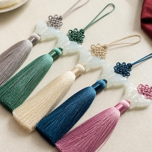 May include: A selection of silk tassels in various colours, including grey, green, cream, teal, and pink. Each tassel features a decorative knot and a butterfly-shaped jade pendant. The pendants are white, and the knots match the tassel colours.