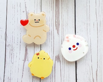 May include: Three resin pins featuring cartoon characters. A white bear holding a red heart, a white cloud with a red smiling mouth and pink cheeks, and a yellow chick with a red bow.