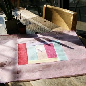 May include: A pink and white patchwork fabric placemat with a geometric design. The placemat is made of a soft, lightweight fabric and is perfect for adding a touch of color and style to any table setting.