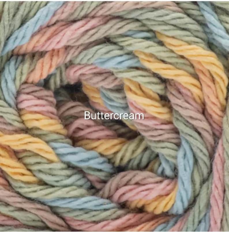 Puede incluir: Primer plano de un ovillo de hilo Buttercream. El hilo es una mezcla de colores pastel, incluyendo azul claro, rosa, amarillo y verde. El hilo est&aacute; bien enrollado, mostrando la textura de las fibras. La palabra "Buttercream" est&aacute; impresa en el hilo.