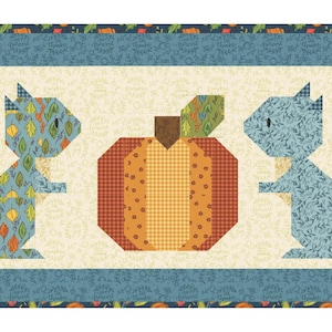 May include: A rectangular quilt featuring two stylized squirrels flanking a pumpkin. The squirrels are in shades of blue and patterned with leaves. The pumpkin is orange and brown. The quilt has a blue border with a cream background.