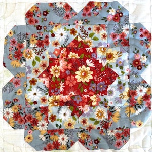 May include: A quilt block with a floral pattern in shades of red, pink, white, and blue. The block is made up of nine smaller squares, each with a different floral design. The block is surrounded by a white border.