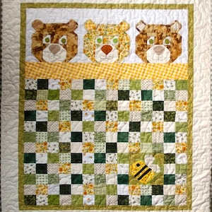 May include: A green, yellow and white patchwork quilt with a bee design in the centre. Three brown bear faces are sewn across the top of the quilt.