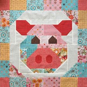 May include: A patchwork quilt block depicting a pig's face. The pig has red ears and snout, brown eyes, and is framed by a white border. The quilt incorporates patterned fabrics in pink, blue, yellow, and floral designs, creating a vibrant composition.