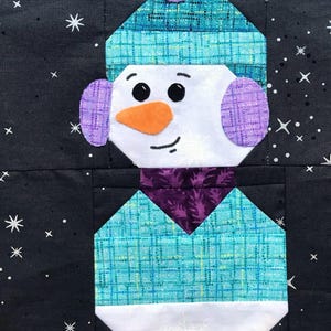 Puede incluir: Un muñeco de nieve de patchwork azul y blanco con un gorro y orejeras moradas. El muñeco de nieve está sobre un fondo negro con estrellas blancas.
