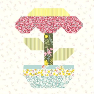 Op de afbeelding: Een kleurrijke patchwork bloem met een groene stengel en bladeren in een blauw-witte gepatroneerde pot. De bloem heeft een geel-roze-rode gepatroneerde kern.