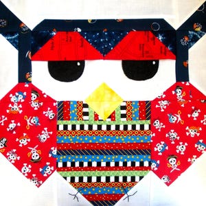 May include: A colorful patchwork quilt block featuring an owl with a pirate eye patch. The owl is made of various fabrics with red, blue, yellow, white, and black colors. The owl's eye patch is red and has a white skull and crossbones design.