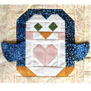 May include: A quilted penguin block with a heart-shaped chest. The penguin features a white body, blue patterned wings, and a blue and white patterned head. The eyes are green, and the beak is orange. The background is a light beige fabric with pink polka dots.