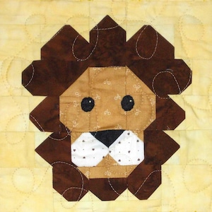 Peut inclure: Un carré de patchwork fait main représentant une tête de lion. La crinière du lion est marron foncé, géométrique, entourant un visage beige avec des yeux noirs et un nez blanc et noir. Le fond est jaune clair avec un motif matelassé.