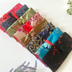 May include: A set of eight colourful silk pouches with intricate patterns and tied with red ribbons. The pouches are made of a soft, luxurious fabric and are perfect for storing small items like jewellery, coins, or other trinkets.