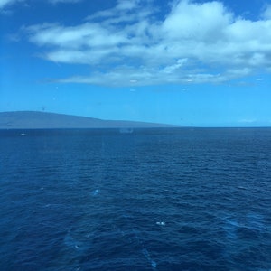 May include: A view of the ocean with a distant mountain range in the background. The sky is blue with white clouds.