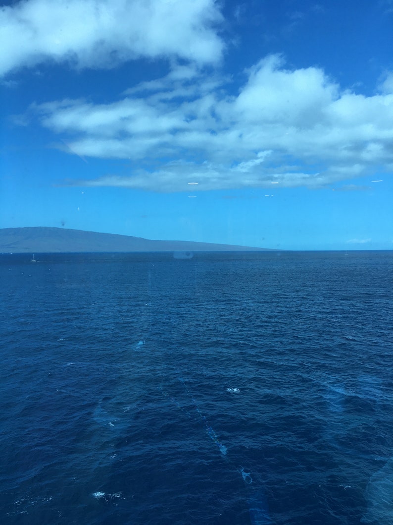 May include: A view of the ocean with a distant mountain range in the background. The sky is blue with white clouds.