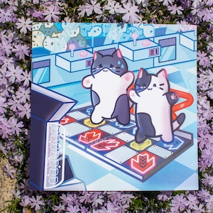 May include: Square print featuring two cartoon cats playing a dance game. The cats are black and white with pink accents, standing on a colorful game board. The background is a light blue arcade setting with other cat characters.