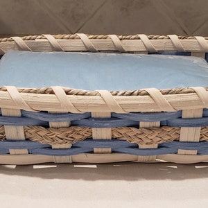 May include: A woven basket with a blue and white pattern. The basket is made of natural materials and has a rectangular shape. It is ideal for holding small items, such as napkins or utensils.