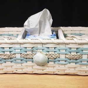May include: White wicker tissue box holder with a blue and tan woven design. The holder has a seashell accent and is divided into three sections.