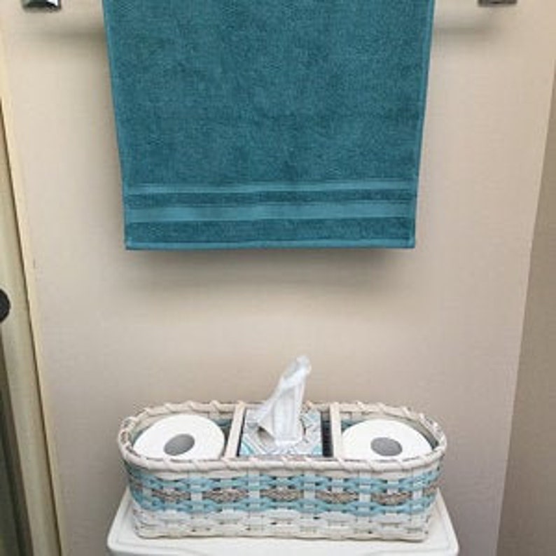 May include: White wicker bathroom storage basket with two rolls of toilet paper and a tissue box dispenser. The basket has a blue and white woven pattern.