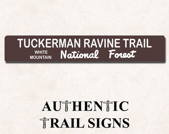 May include: A rectangular brown trail sign with white text reading TUCKERMAN RAVINE TRAIL and WHITE MOUNTAIN National Forest. Below the sign, the black text reads AUTHENTIC TRAIL SIGNS with small trail sign icons replacing the letter I.